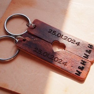 May include: A brown leather keychain with two key rings and a heart cutout. The keychain is engraved with the date "25.01.2024" and the text "M&Mrs H".