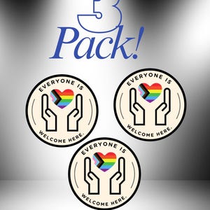 May include: A 3 Pack of circular stickers featuring a cream background with a black outline of two hands cupping a rainbow-coloured heart. The text "EVERYONE IS WELCOME HERE." is printed in black around the top and bottom of the sticker design.
