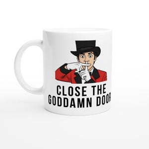 May include: White ceramic mug featuring a cartoon illustration of a magician in a red jacket, black top hat, and white gloves, with the text "CLOSE THE GODDAMN DOOR" in black letters.