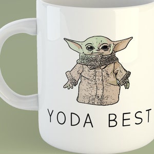 May include: White ceramic mug with a cartoon image of a green alien character wearing a brown coat and the text "Yoda Best" printed on the front.