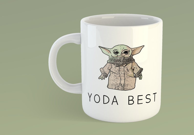 May include: White ceramic mug with a cartoon image of a green character wearing a brown coat and a scarf. The text "YODA BEST" is printed in black below the image.