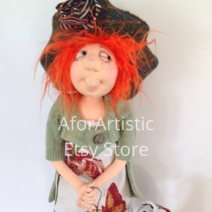 May include: A handmade doll with red hair, a green sweater, and a floral skirt. The doll is holding a leash attached to a small white and black dog.