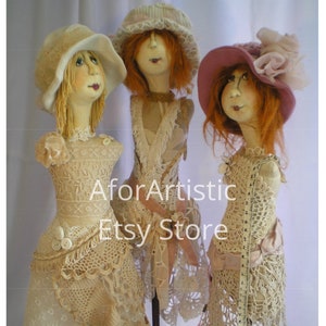 May include: Three vintage-style dolls with crocheted dresses and hats. The dolls are made of fabric and have painted faces. They are standing on wooden bases.