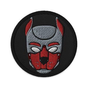 以下が含まれることがあります： 赤い鼻と白い目をした犬のマスクが描かれた、黒と赤の刺繍パッチ