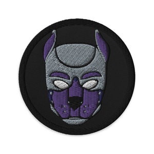 Op de afbeelding: Een ronde, zwarte geborduurde patch met een grijs en paars hondenmaskerontwerp. Het masker heeft een puntige snuit, grote ogen en een paarse snuit.