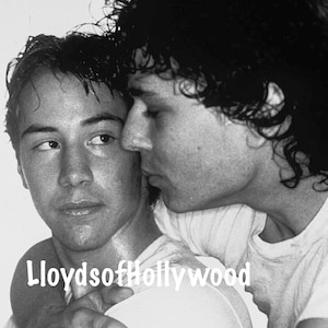 May include: Black and white photograph featuring two men embracing. One man is looking to the side, while the other is leaning in close. The image has the text "LloydsofHollywood" in the center.