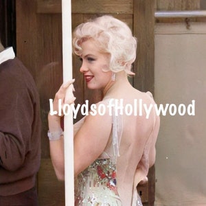 May include: A woman with blonde hair wearing a sequined dress with a low back. The dress has a light green, white, and pink pattern. The woman is standing next to a wooden door.