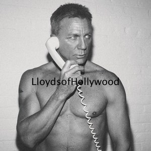 May include: A black and white photo of a man with a bare chest holding a white rotary phone to his ear. The phone cord is coiled around his arm. The text "LloydsofHollywood" is visible in the image.