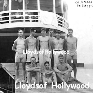 Puede incluir: Fotografía vintage en blanco y negro de la tripulación de Columbia de Poughkeepsie. Nueve hombres posan en un muelle de madera, algunos de pie y otros sentados. Los hombres visten trajes de baño y pantalones cortos. Un barco está al fondo.