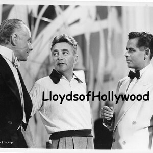 May include: Black and white photograph of three men in formal attire. One man wears a tuxedo with a bow tie, another a white polo shirt, and the third a white suit with a bow tie. The image is a vintage Hollywood portrait.