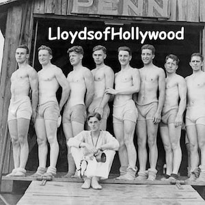 Puede incluir: Una fotografía en blanco y negro de un grupo de ocho hombres de pie frente a un edificio de madera. Los hombres llevan bañadores y sonríen. El texto "Lloyds of Hollywood" está escrito encima de ellos.