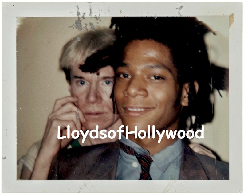May include: A black and white photo of two men, one with short blond hair and the other with long black hair. The man with blond hair is wearing a white shirt and a brown jacket. The man with black hair is wearing a blue shirt with a red and black tie. The text "LloydsofHollywood" is printed on the bottom of the photo.