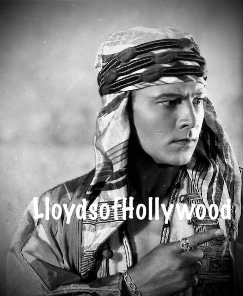 May include: Black and white vintage photograph of a person wearing a patterned headscarf and a decorative ring. The image has the text "Lloyds of Hollywood" in the lower left corner. The person is looking off to the side.