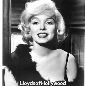 May include: Black and white portrait of a woman with blonde hair wearing a black fur stole and a black strapless dress. The woman is smiling and looking at the camera. The image is captioned "Lloyds of Hollywood".
