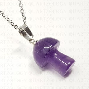 Pode incluir: Um colar com pingente de cogumelo roxo. O pingente &eacute; esculpido em uma pedra polida de cor ametista e &eacute; preso a uma corrente prateada. O colar &eacute; exibido em um fundo branco com a palavra "QUARTZOLOGY" repetida.