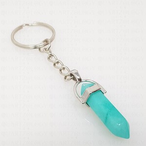 May include: A silver keyring with a light blue crystal pendant. The crystal is shaped like a point and has a silver cap on the top.