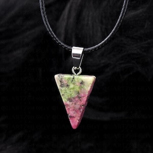 May include: A triangular pendant made of a pink, green, and white stone, suspended from a black cord. The pendant is attached to a silver-coloured metal bail. The background is black.
