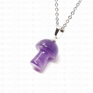 Pode incluir: Um colar com pingente de cogumelo de ametista roxa. O pingente em forma de cogumelo &eacute; esculpido em uma pedra preciosa roxa transl&uacute;cida e &eacute; suspenso por uma corrente prateada. O colar &eacute; uma pe&ccedil;a de joalheria &uacute;nica.
