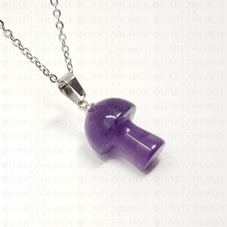 Pode incluir: Um colar com pingente de cogumelo roxo. O pingente &eacute; esculpido em uma pedra polida de cor ametista e &eacute; preso a uma corrente prateada. O colar &eacute; exibido em um fundo branco com a palavra "QUARTZOLOGY" repetida.