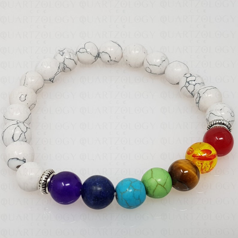 Puede incluir: Un brazalete de cuentas blancas con siete piedras de chakra. Las piedras son moradas, azules, turquesas, verdes, marrones, amarillas y rojas. El brazalete est&aacute; hecho de cuentas blancas con vetas negras.