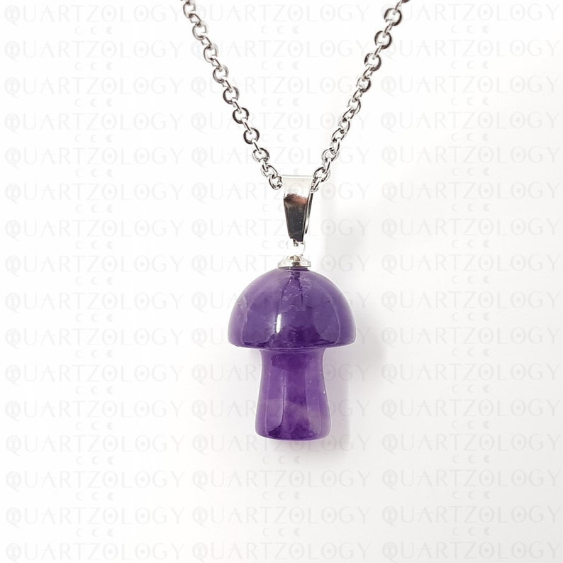Pode incluir: Um colar com pingente em forma de cogumelo. O pingente &eacute; feito de ametista roxa polida e &eacute; suspenso por uma corrente prateada. O colar &eacute; exibido em um fundo branco com a palavra "QUARTZOLOGY" repetida.