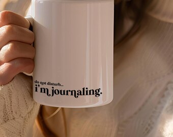 May include: White ceramic mug with black text that reads "do not disturb... i'm journaling."