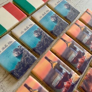 May include: A selection of decorated biscuits. Some are decorated with the Italian flag, others with a coastal scene and the text "La Bella Vita", and others with wine bottles and glasses. The biscuits are rectangular.