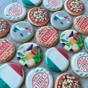 May include: A selection of round biscuits decorated with Italian motifs. Designs include the Italian flag, a map of Italy, pizza, and the words "ITALIA" or "MADE IN ITALY". The biscuits have a white icing base.