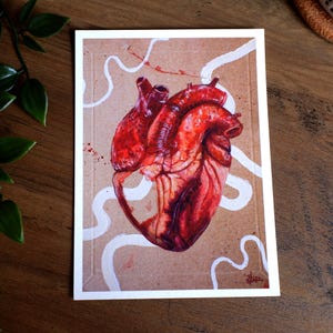 Könnte beinhalten: Anatomischer Kunstdruck mit einer detaillierten Illustration eines menschlichen Herzens. Das Herz ist in Rot- und Brauntönen dargestellt, mit weißen, wellenförmigen Linien und roten Spritzern auf einem beigen Hintergrund. Das Kunstwerk ist in einem weißen Rahmen eingefasst.