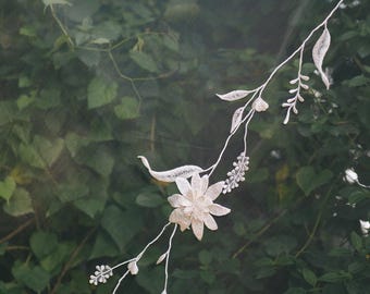 May include: White floral embroidery on a sheer fabric, resembling a vine with leaves and flowers. The embroidery is against a dark green background.