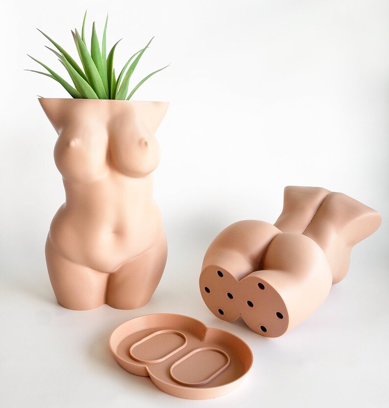 May include: Two nude-colored ceramic planters shaped like the human body. One planter has a plant growing out of the top. The other planter has drainage holes on the bottom. A matching nude-colored ceramic tray is included.