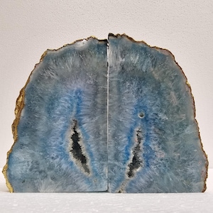 Op de afbeelding: Twee bijpassende agaat boekensteunen. Elke boekensteun heeft een halfronde vorm met een blauw en wit interieur en een goudkleurige rand. De boekensteunen hebben een natuurlijke, organische uitstraling en staan tegen een witte achtergrond.