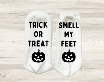 May include: A pair of white socks with a black pumpkin and text. One sock says "Trick or Treat" and the other says "Smell My Feet".