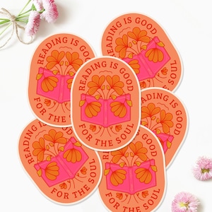 Pode incluir: Seis adesivos ovais cor de p&ecirc;ssego com o texto "Ler &eacute; bom para a alma" em uma fonte retr&ocirc;. Cada adesivo apresenta um livro aberto rosa com flores laranja crescendo dele.