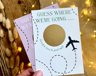 May include: Two cards with the text "GUESS WHERE WE'RE GOING..." are displayed. One card is white with a gold scratch-off circle and a black airplane graphic. The other card is lavender. The text "Scratch here to find out!" is also visible.