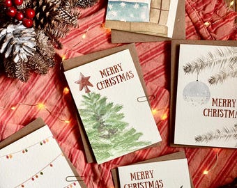 Può includere: Cinque biglietti d'auguri rettangolari con carta bianca e retro in cartoncino marrone, ognuno con illustrazioni ad acquerello di temi natalizi tra cui regali, un pino, ornamenti, luci e un pudding con il testo Merry Christmas.