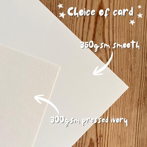 May include: Two sheets of cardstock with text reading Choice of card, 350gsm smooth, and 300gsm pressed ivory. One sheet is a smooth white cardstock, and the other is a textured ivory cardstock, both displayed for comparison of paper quality.