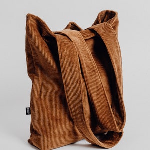 Könnte beinhalten: Eine braune Cordtasche mit langen Henkeln. Die Tasche hat ein kleines schwarzes Etikett mit dem Text "MADE IN ITALY".