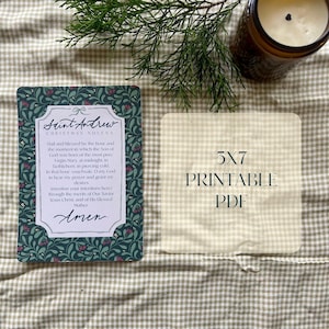 May include: A rectangular card with the text "Saint Andrew Christmas Novena" in a decorative font, surrounded by a floral border. Beside it is a 5x7 inch printable PDF card. A lit candle and greenery are in the background.