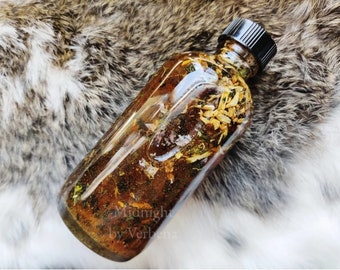 May include: A clear glass bottle filled with a brown liquid and dried herbs and flowers. The bottle has a black lid and the label reads "Midnight by Verbena".