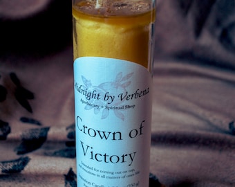 May include: A clear glass jar candle with a yellow wax and a white label that reads "Midnight by Verbena Apothecary + Spiritual Shop Crown of Victory Intended for coming out on top, and victorious in all matters of ones life Intention Candle | 8.1 oz (230 g) Prepared in Long Beach, MS"