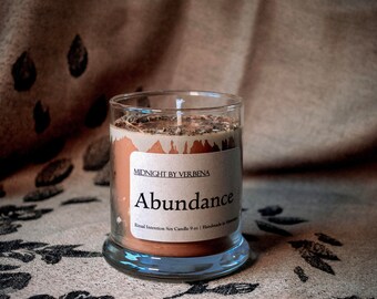 May include: A brown glass candle jar with a white label that reads "Midnight by Verbena Abundance Ritual Intention Soy Candle 9 oz | Handmade in Baltimore".