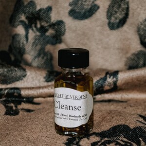 May include: A small glass bottle with a black cap filled with a clear liquid and herbs. The label reads "NIGHT BY VER BENA Cleanse  Handmade in MS  Oil 3 fl oz | External Use Only".
