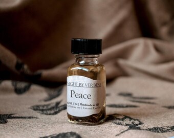 May include: A small glass bottle with a black cap filled with a light brown liquid. The bottle has a white label with the text "NIGHT BY VER BEN" and "Peace" printed on it. The bottle is sitting on a brown fabric surface.