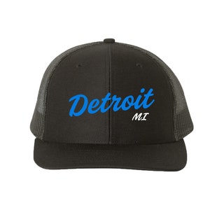 Op de afbeelding: Zwarte truckercap met een blauw geborduurd, cursief "Detroit MI" logo.