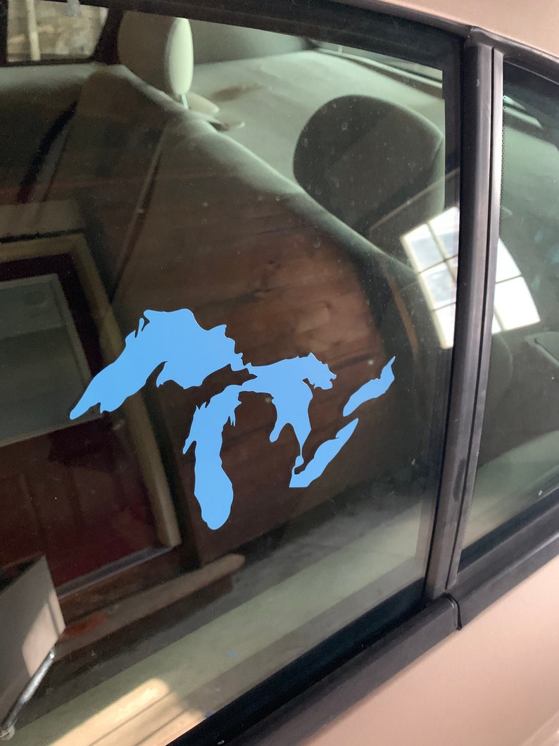 Op de afbeelding: Een blauwe vinyl sticker van de Grote Meren op een autoruit.