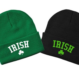 Op de afbeelding: Twee gebreide mutsen, een groene en een zwarte, met het woord "IRISH" in witte letters en een groene klaver op elk.