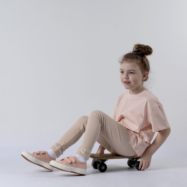 Model sitting on a wooden skateboard with a close up of the Aneby leggings with trendy hem tag