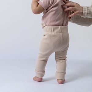 Small baby attempting to stand whilst modelling the beige Aneby leggings
