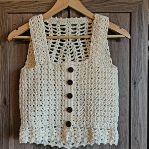 May include: A crocheted cream-colored sleeveless vest with a button closure and a delicate openwork design on the back.